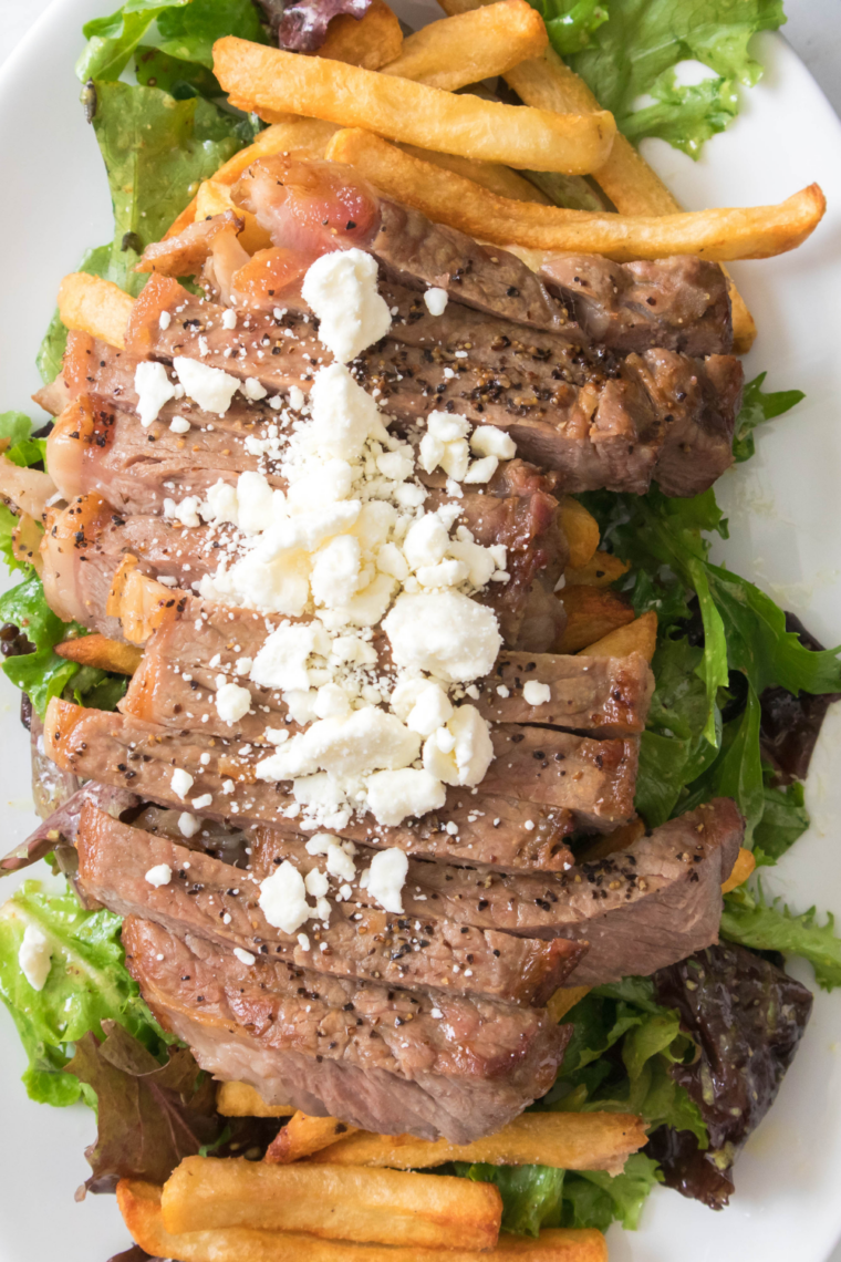 Air fryer-cooked steak served with crispy golden fries and fresh salad, garnished with herbs.