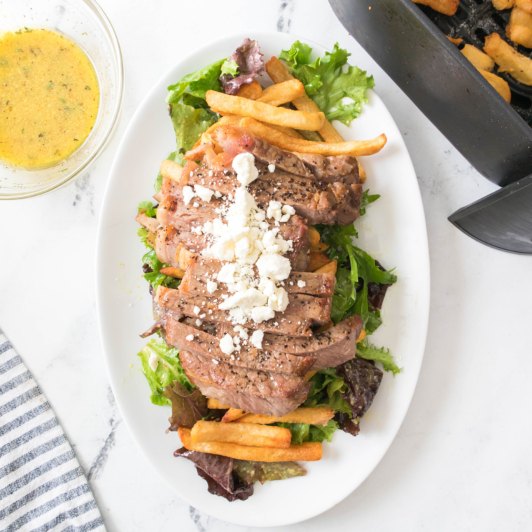 Juicy air fryer steak served with crispy golden fries and fresh greens, garnished with herbs.