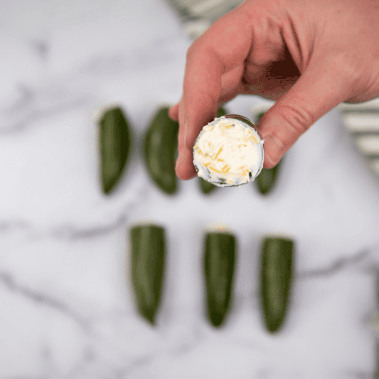 Jalape&ntilde;os stuffed with cream cheese, wrapped in seasoned meat and bacon, secured with toothpicks.