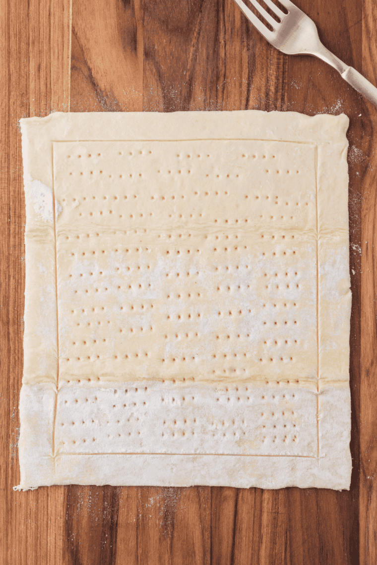 Puff pastry sheet being rolled out on a floured surface.