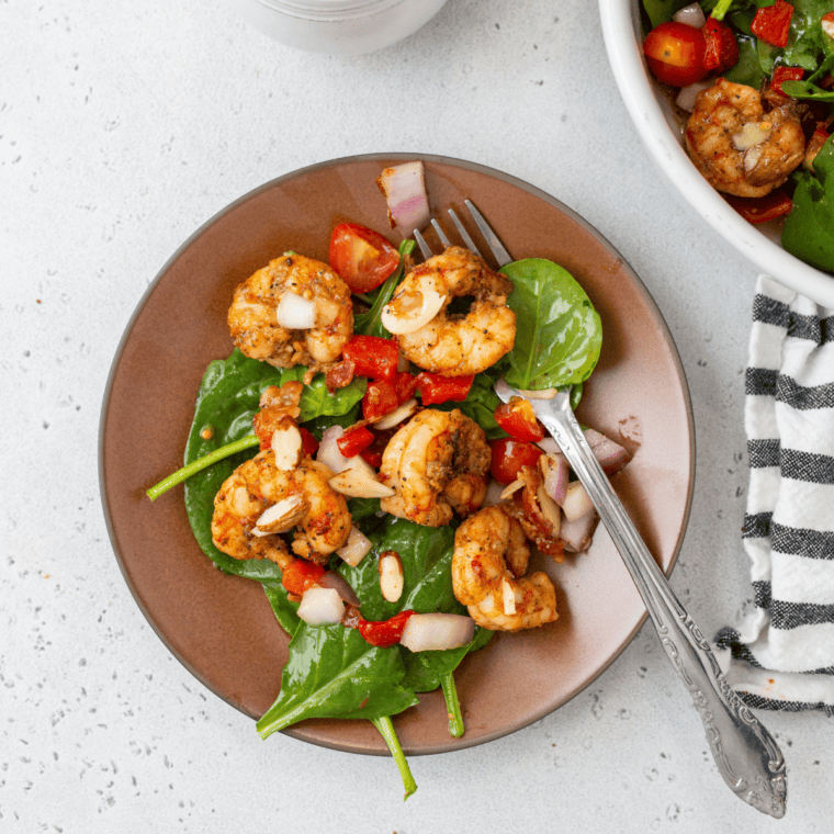 Air fryer shrimp served over fresh spinach with a light dressing in a bowl.