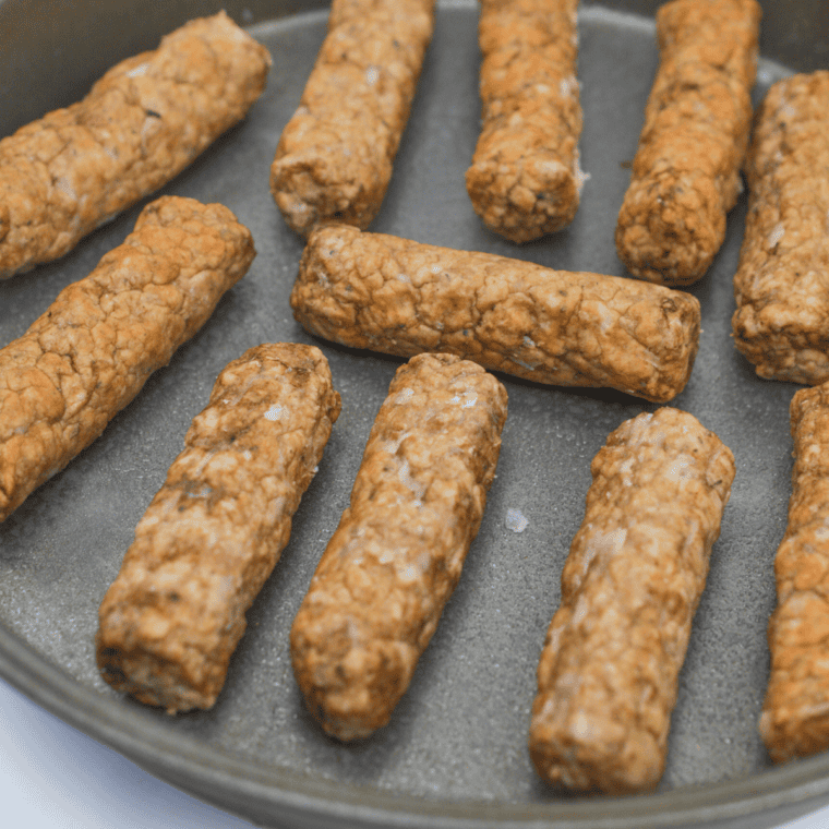 Pork sausages pricked with a fork arranged in a small metal dish with vegetable oil ready for the air fryer