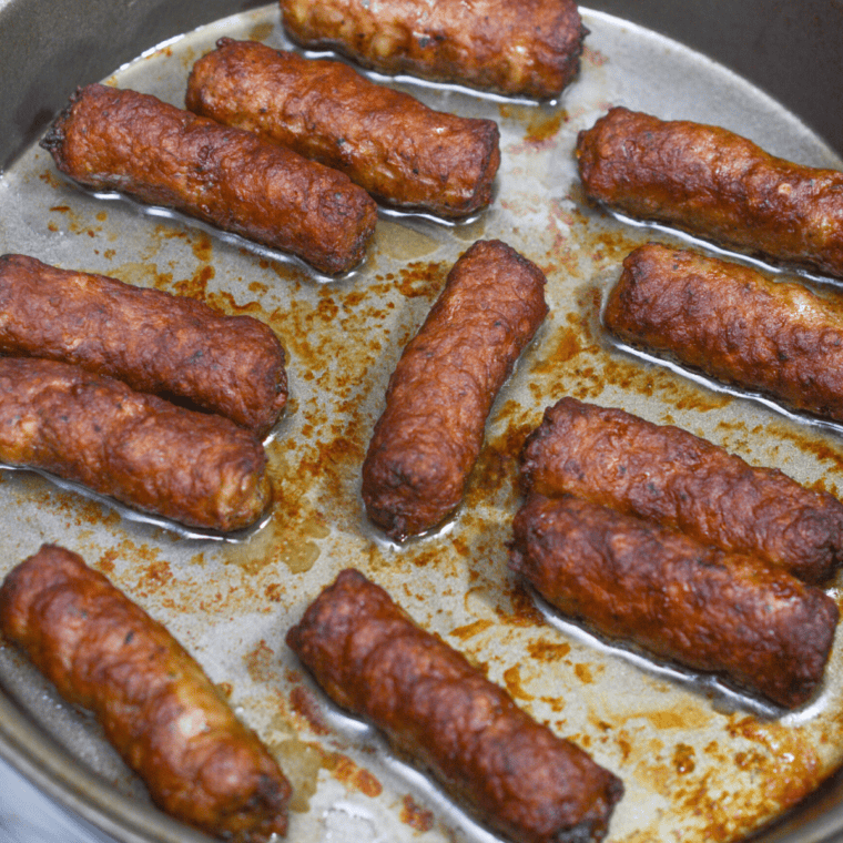 Browned pork sausages sizzling in hot fat inside a metal dish in the air fryer basket