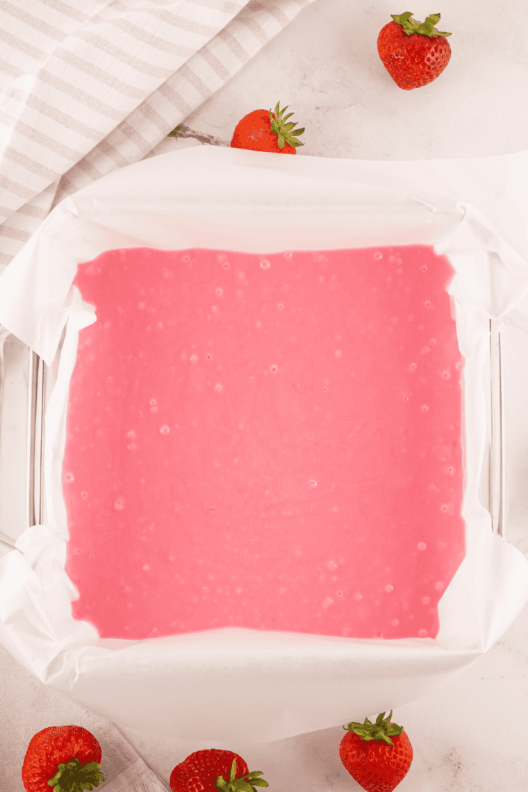 Smooth pink strawberry fudge mixture spread evenly in a parchment-lined pan.