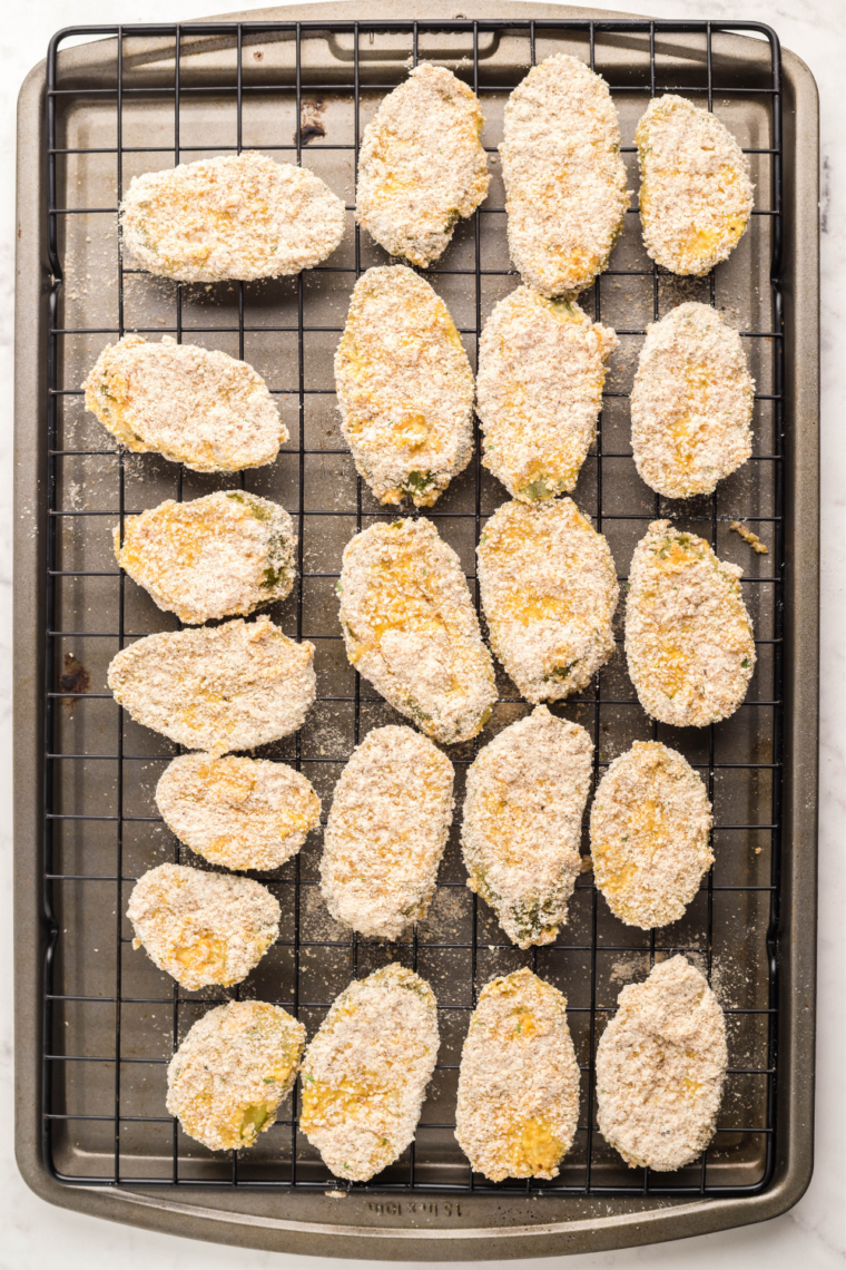 Breaded dill pickle chips resting on a wire rack before air frying
