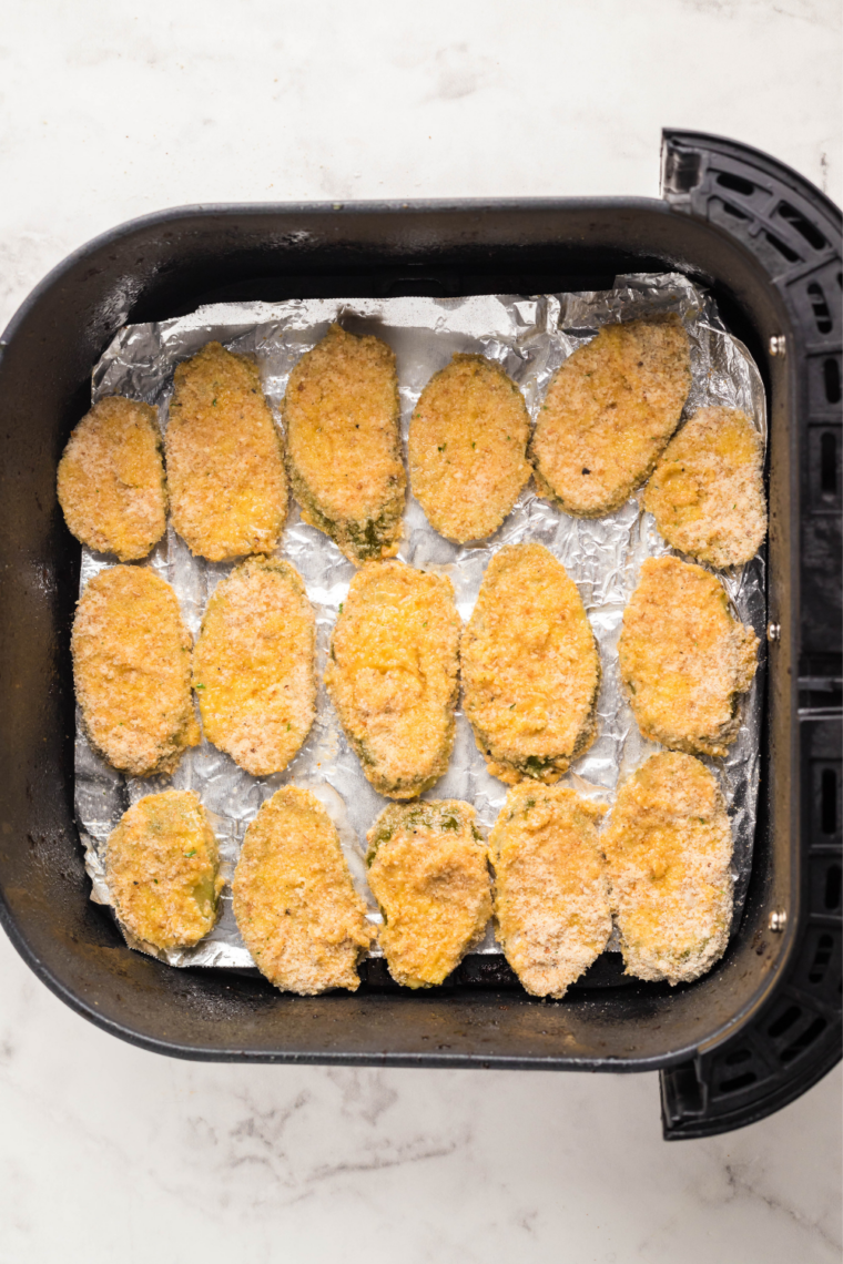 Uncooked breaded pickle chips arranged in a single layer in an air fryer basket