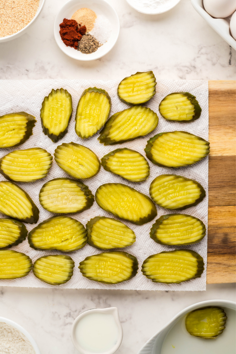 Drained dill pickle chips laid out in rows on paper towels to remove excess moisture