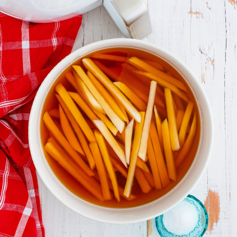 "Shoestring fries being tossed in a bowl with melted beef tallow and salt"