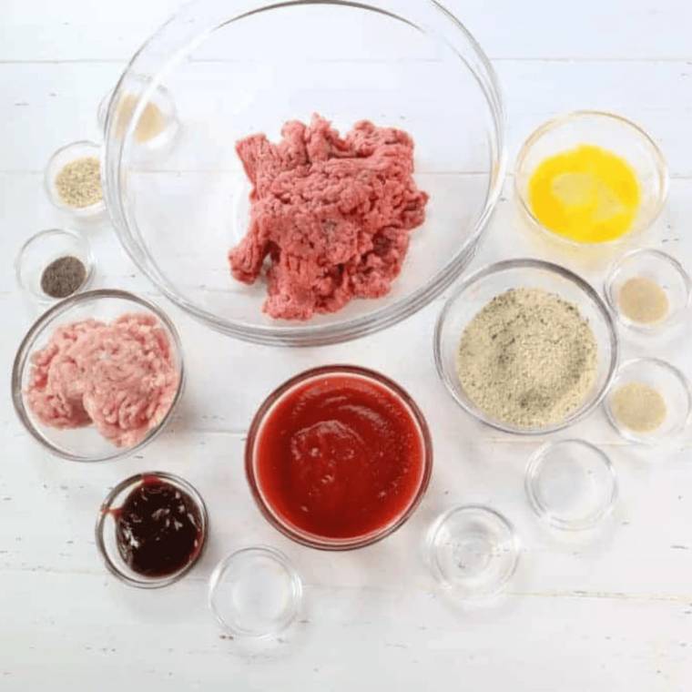Ingredients for copycat Bob Evans meatloaf including ground beef, ground pork, saltine crackers, eggs, milk, onion, green pepper, and signature glaze ingredients on a countertop