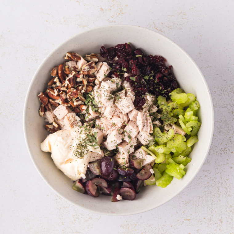 Finely diced celery, sliced green onions, dried cranberries, and chopped pecans on a cutting board