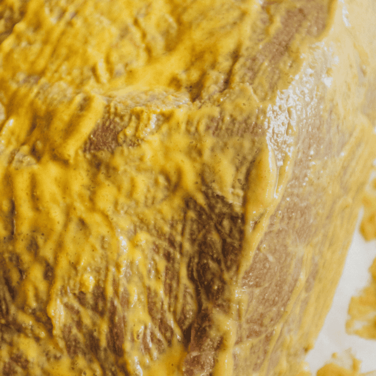 Patting salt and pepper brisket rub onto all sides of a raw brisket