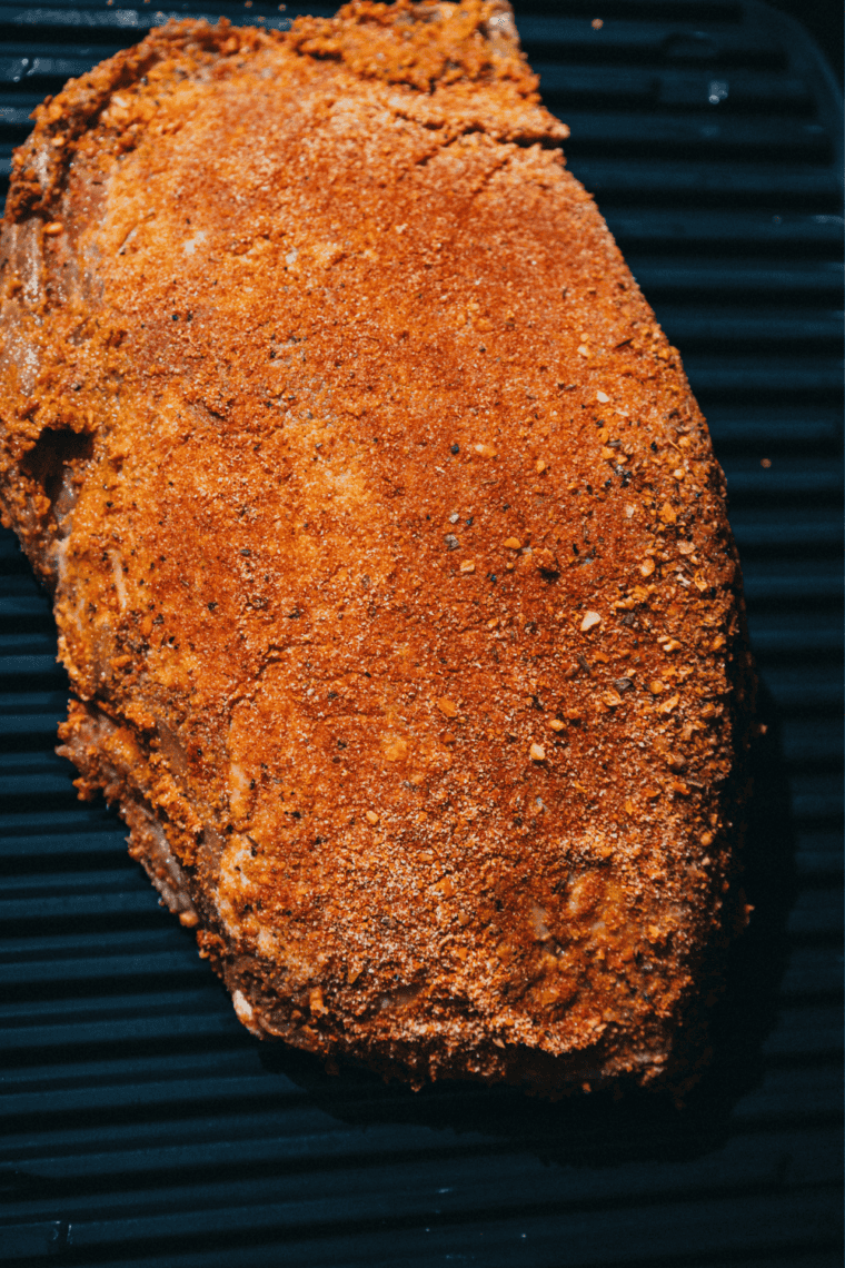 Seasoned brisket cooking on a smoker grate with light smoke