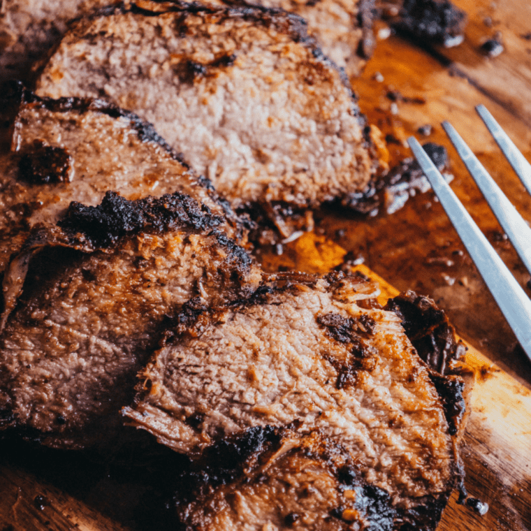 Copycat Buc-ee's brisket sliced on a wooden cutting board with a dark peppery bark
