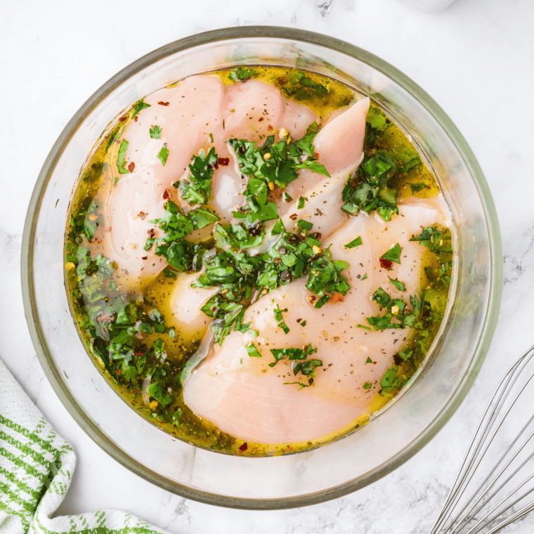 Chicken breast between plastic wrap being pounded to an even thickness with a meat mallet