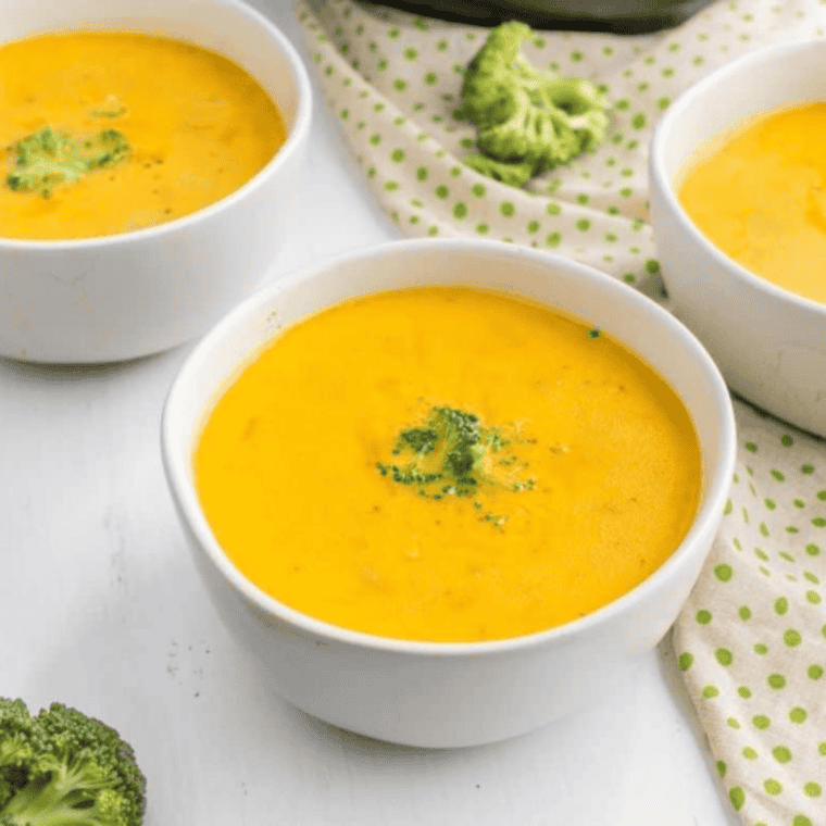 Copycat Denny's broccoli cheese soup in a white bowl topped with shredded cheddar