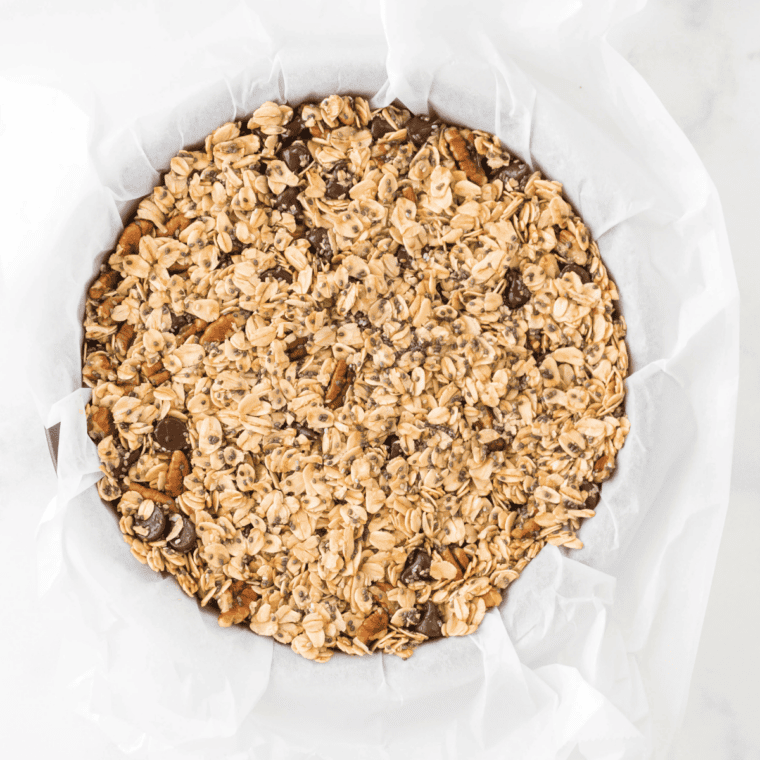 Granola mixture pressed into an even layer on parchment paper in an air fryer basket