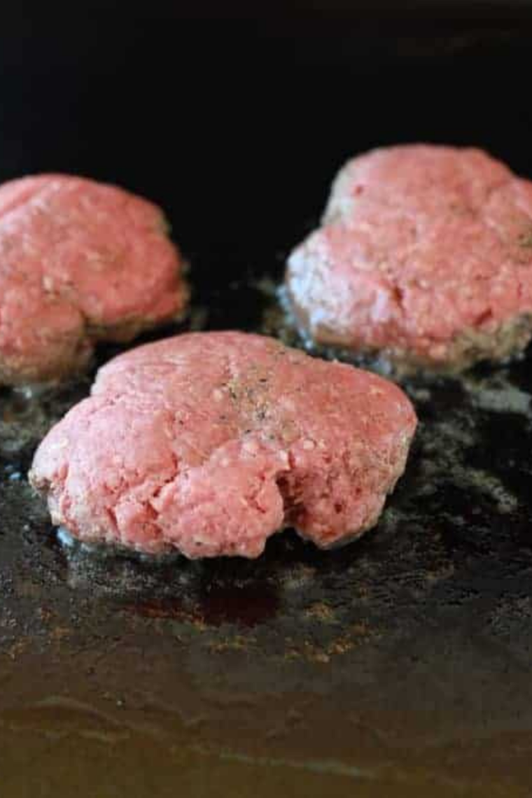 Beef ball being smashed thin on a hot griddle with a burger press and parchment paper