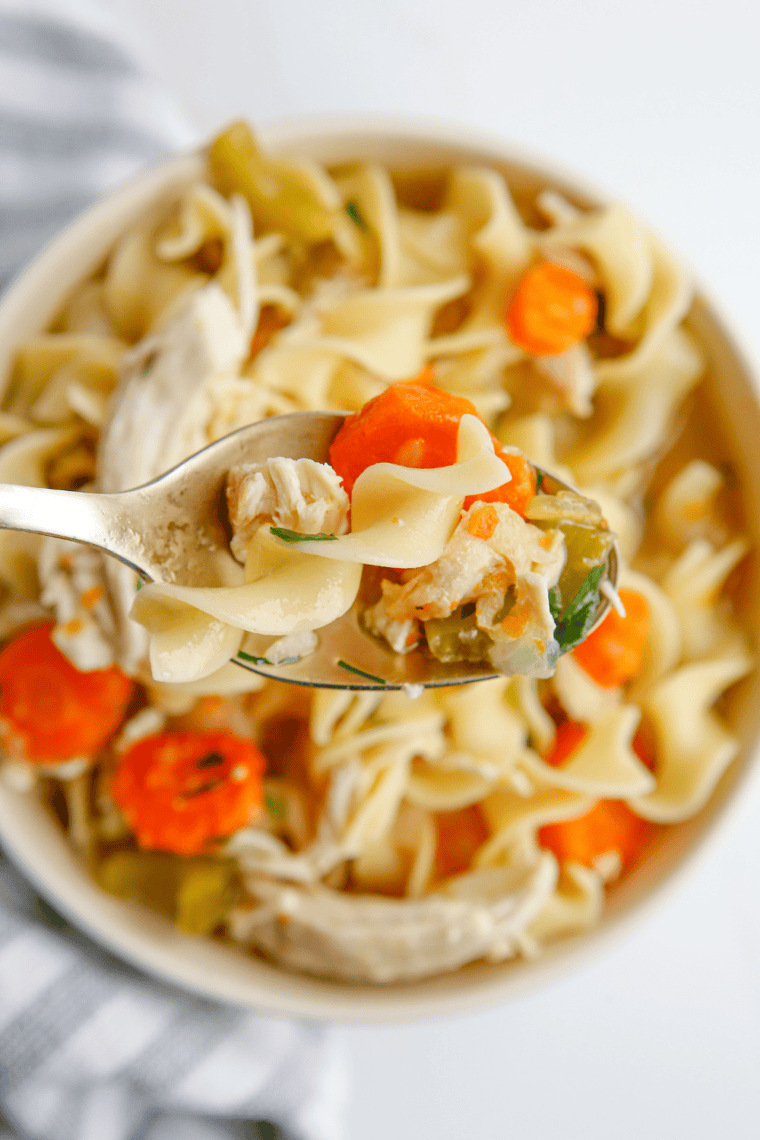 Overhead view of homemade Denny's chicken noodle soup in a white diner-style bowl with crackers on the side