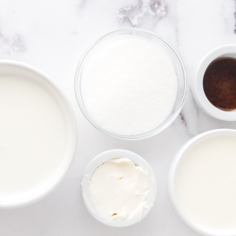 Ingredients for a birthday cake milkshake, including heavy cream, milk, sugar, cream cheese, vanilla, frosted yellow cake, and rainbow sprinkles