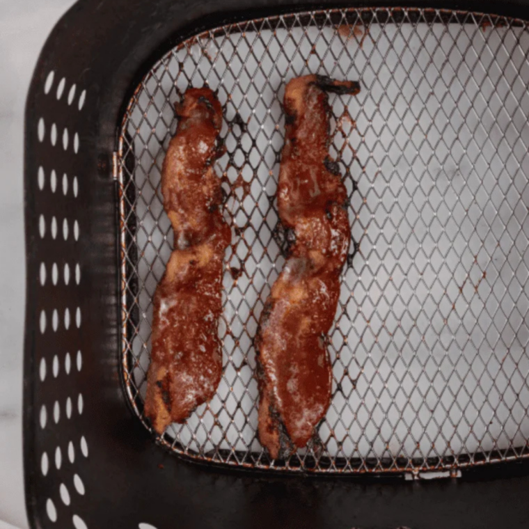 Brown sugar bacon cooking in an air fryer basket on a perforated parchment liner