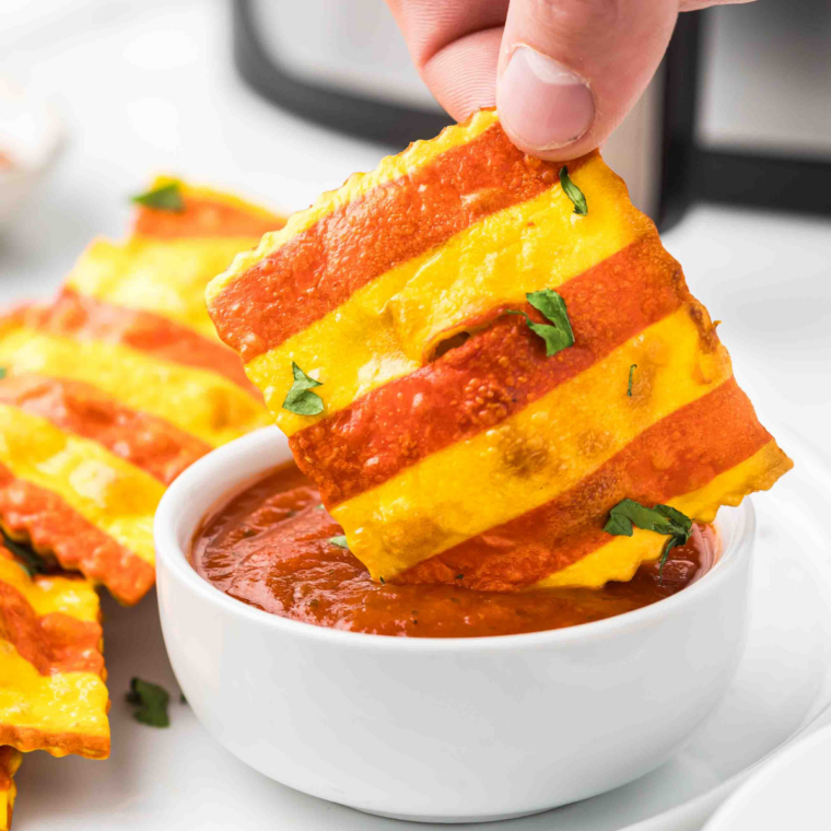 Finished marinara dip in a ramekin next to a plate of air fryer ravioli.
