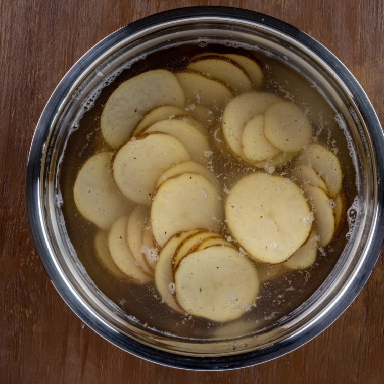 Sliced russet potatoes soaking in a bowl of cold water to remove starch for crispy chips