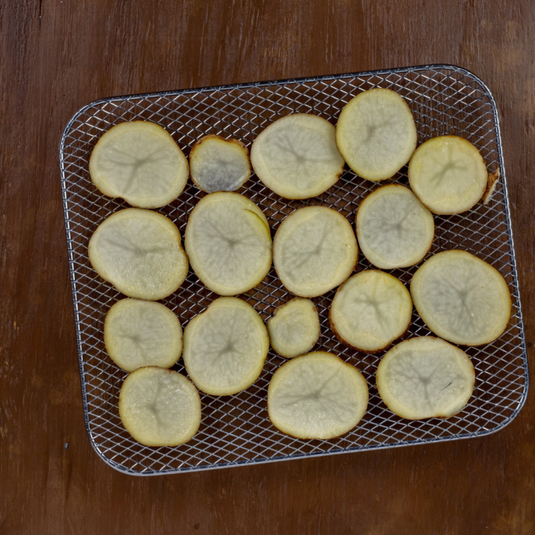 Thick-cut potato chips in the air fryer basket, curling and browning at the edges