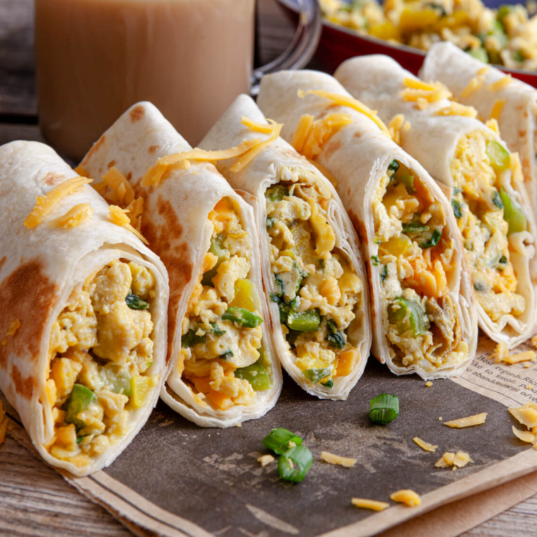 Close-up of a copycat Buc-ee's breakfast burrito sliced in half, showing fluffy scrambled eggs, crumbled sausage, and melted cheddar cheese