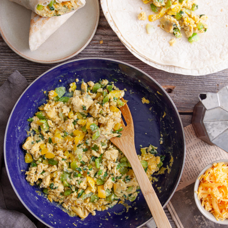 Assembling a breakfast burrito with cheese, scrambled eggs, and crumbled sausage on a flour tortilla