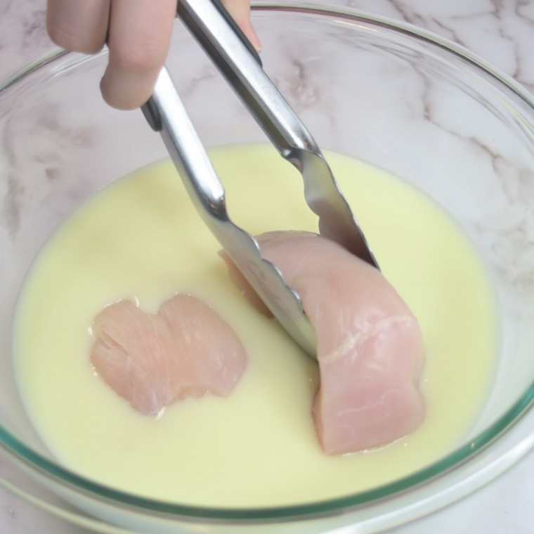 Chicken cutlets marinating in a bowl of buttermilk and hot sauce