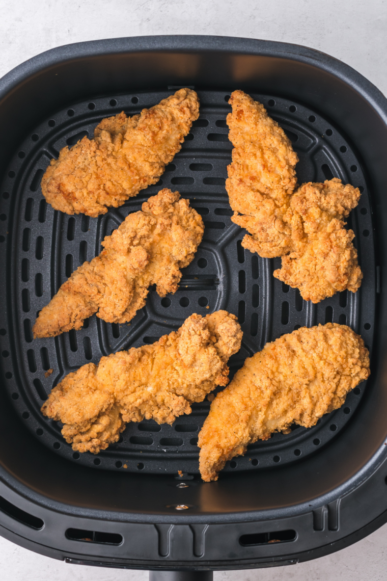 Breaded chicken fillets in an air fryer basket sprayed with oil before cooking