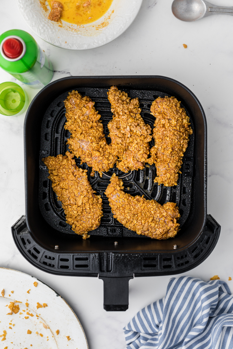 Breaded Hardee&rsquo;s copycat chicken tenders in an air fryer basket sprayed with oil