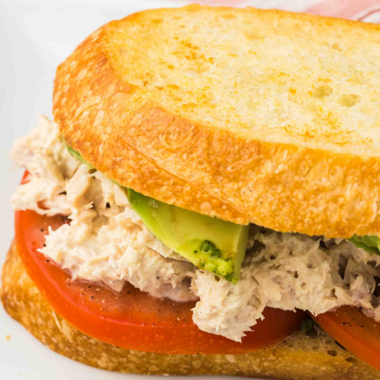 Tuna salad spread on a sliced sub roll topped with cucumber and tomato slices