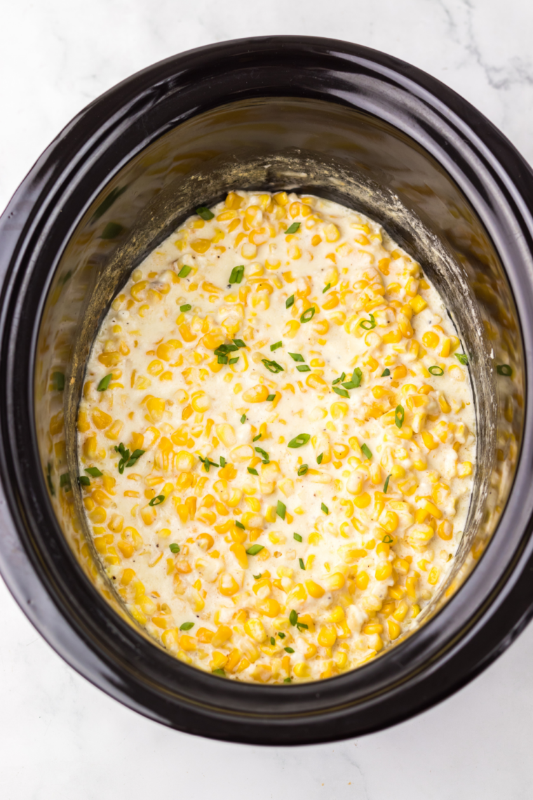 Frozen corn topped with heavy cream and cubed butter in a crockpot before cooking.