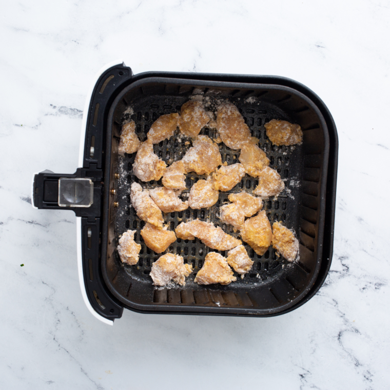 Breaded boneless wings in a single layer in an air fryer basket, sprayed with oil.