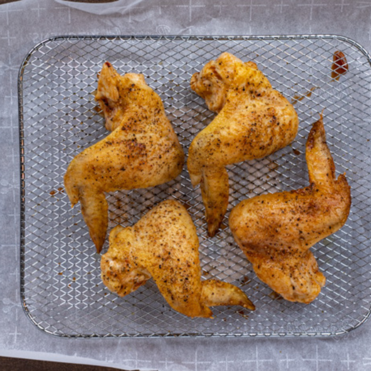 Golden, crispy chicken wings in the air fryer basket after cooking.