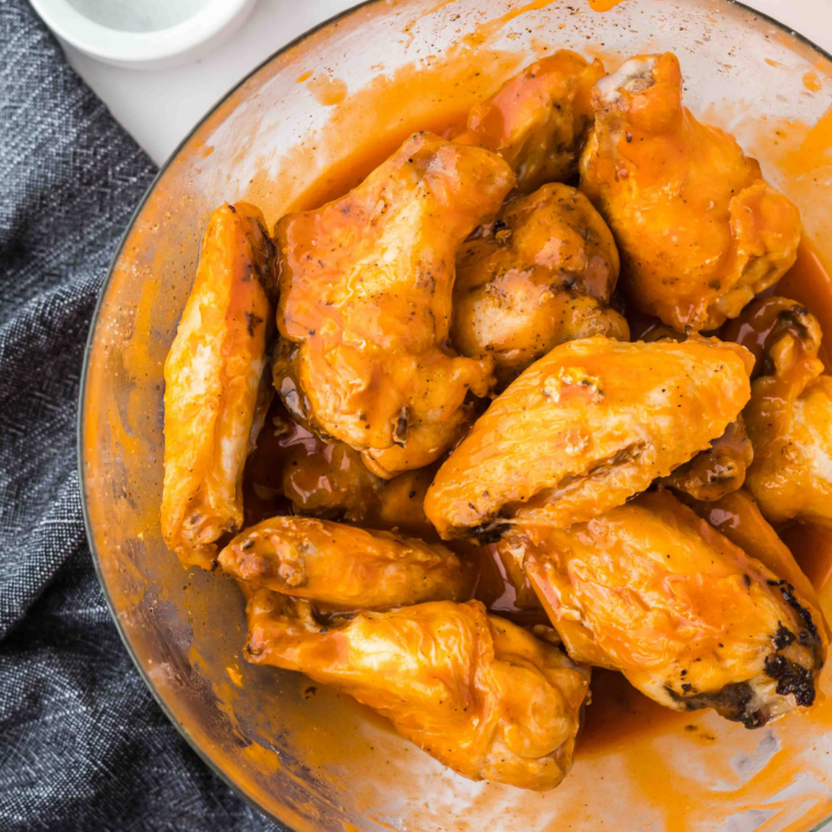 Crispy wings being tossed in sweet chili sauce in a large bowl.