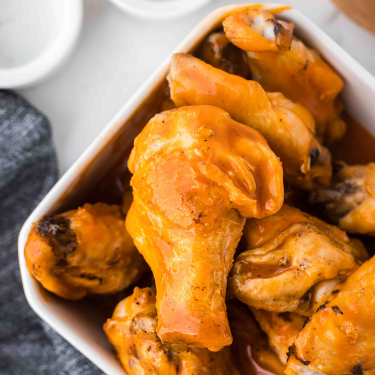 Crispy wings being tossed in sweet chili sauce in a large bowl.