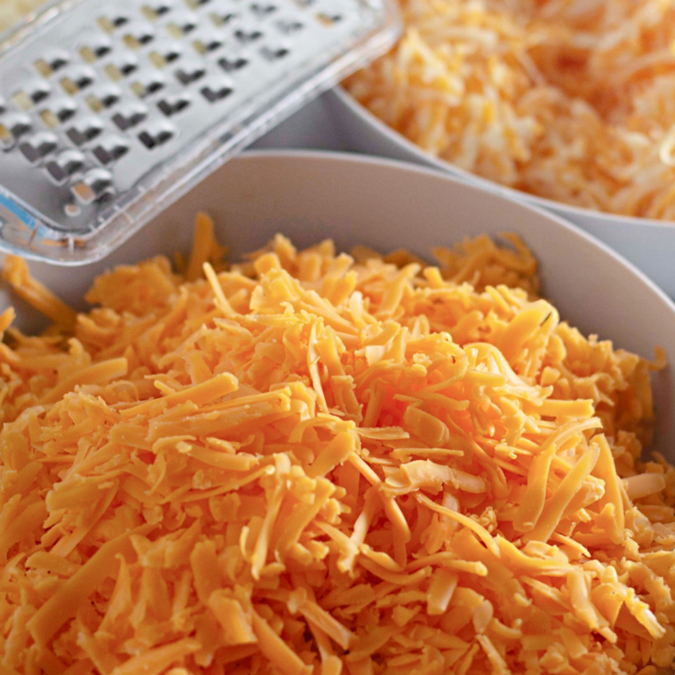 Shredded Wisconsin cheddar melting into creamy cheese sauce over low heat