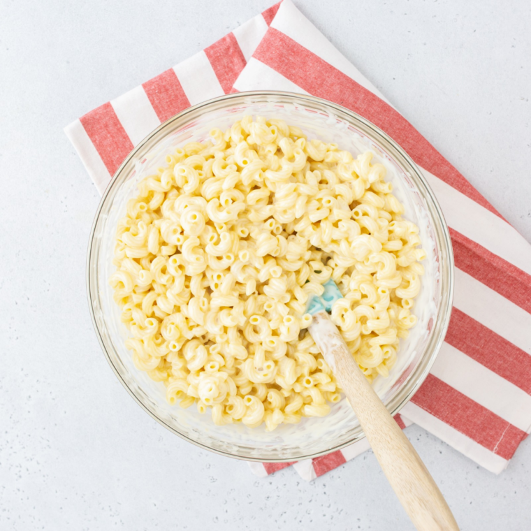 Cooked macaroni being stirred into smooth cheddar cheese sauce