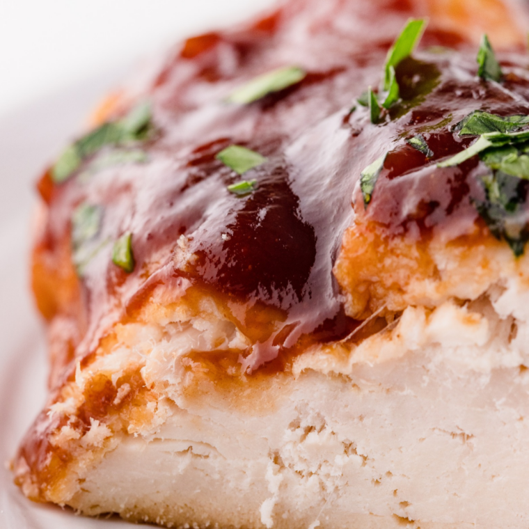 Sliced barbecue chicken breast in a glass meal prep container with BBQ sauce spooned over it