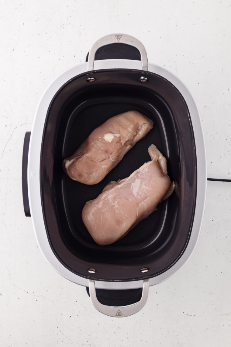 Dry-rubbed chicken breasts arranged in a single layer over sliced onions in a 6-quart slow cooker