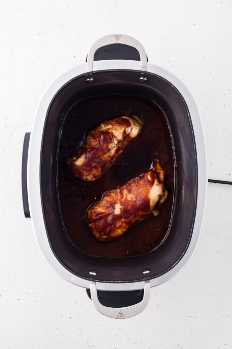 Instant-read thermometer reading 165°F in the thickest part of a barbecue chicken breast in the slow cooker