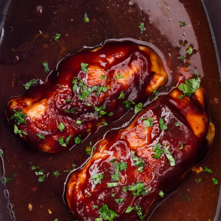 Slow cooker barbecue chicken breast sliced against the grain with thickened BBQ sauce spooned over the top