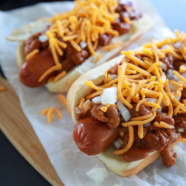 Copycat Sonic chili spooned over grilled hot dogs in toasted buns, topped with shredded cheddar and diced onion
