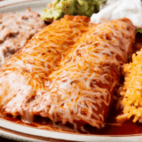 Instant Pot chicken enchiladas topped with melted cheese, sour cream, and fresh cilantro in a baking dish