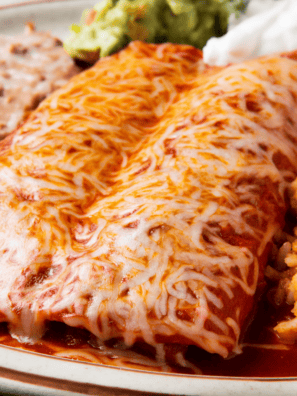 Instant Pot chicken enchiladas topped with melted cheese, sour cream, and fresh cilantro in a baking dish