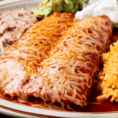 Instant Pot chicken enchiladas topped with melted cheese, sour cream, and fresh cilantro in a baking dish