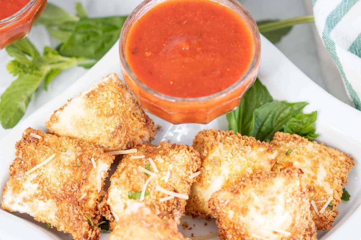 Can I Make Air Fryer Frozen Toasted Ravioli In The Oven? Yes, prepare them, and then instead of putting them into the air fryer, place them into a preheated 400 degrees F for 12-15 minutes.  Making them in the oven is an excellent idea if you make a massive batch of them for a party or get-together.  Can I Make Use Fresh Ravioli? Yes, change the air frying time to about 3-5 minutes, as they will cook faster than the frozen ones.  Next time you are at the store, look around in both the freezer section and the grocery store’s refrigerator section. You will be amazed at all of the different varieties now available.  What Are Some Dips To Go With Air Fried Raviolis? Here are some of my favorites,  Alfredo sauce Ranch Dressing Pesto Sauce Marinara Sauce (A Great Recipe for the Instant Pot Homemade Marinara Sauce) Any sauce you like will be a great dipping sauce, even if you want to add some garlic and melted butter in a small saucepan.    Optional toppings: Grated Parmesan cheese, or mozzarella cheese, and fresh herbs!  Can I Use Filled Ravilois With Meat? Yes, you can use whatever stuffed ravioli you would like. I often change between cheese and meat.  There are so many different varieties now available in the supermarket. Whether fresh or frozen, they are excellent in the air fryer.  How Long To Cook Frozen Toasted Ravioli In Air Fryer Add the frozen ravioli to the air fryer basket; a d then set the temperature to 350 degrees F for 6 minutes. Make sure they are fully cooked before you remove them from your air fryer basket.    How To Cook Frozen Louisa Toasted Ravioli In Air Fryer Place the frozen ravioli in the air fryer basket, and then spray with olive oil, or brush with vegetable oil.  Set the temperature to 350 degrees F, air fryer setting, and air fry for about 5-7 minutes.  What If My Breaded Ravioli Looks Dry? This is a great recipe, and with a few sprays of olive oil, it will come out perfectly toasted and never dry. If it does come out dry, reduce the temperature, and spray halfway with olive oil (or cooking spray)  How To Reheat Ravioli in Air Fryer If you have any leftover toasted ravioli, add them to the air fryer basket, and then spray them with olive oil.  Air fry for about 3-4 minutes, at 380 degrees F, until the toasted ravioli is heated through.  How To Reheat Frozen Toasted Ravioli In the Air Fryer Now that they have frozen air fryer toasted ravioli products to make them, they are already breaded for you.  You can toss them into the air fryer and then set the temperate to 350 degrees F and air fry for about 3-5 minutes.  Some of the ones I have tried at Pioneer Woman’s that come in the freezer have been found at Costco and my local grocery store. (Both in the freezer section)  Can You Freeze Air Fryer Fried Raviolis? Yes. Just bring them to room temperature, then place them into a Ziploc bag, or an airtight container, and store them for up to 2 months.  To Reheat From Frozen: Set them into your air fryer at 350 degrees F and cook time for 8 minutes, flipping halfway.  More Air Fryer Recipes: EASY AIR FRYER, CRISPY RED-PEPPER JELLY WINGS AIR FRYER, FRIED SALAMI CHIPS (KETO FRIENDLY) AIR FRYER BOSTON BROWN BREAD HOW TO MAKE FROZEN HAMBURGERS IN THE AIR FRYER Air Fryer Southwest Egg Rolls Air Fryer Crispy Chicken Wings Air Fryer Olive Garden Chicken Parmesan If you have been looking for a new air fryer ravioli recipe or new favorite appetizers, I hope that you will try this, remember to leave a star rating after trying this recipe!