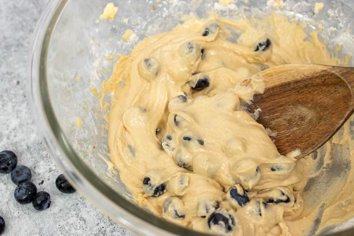 Muffin batter and blueberries mixed in a glass bowl